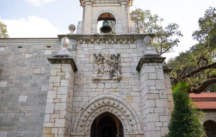 Historic stone building with a decorative arch and bell tower. Trees in the background.