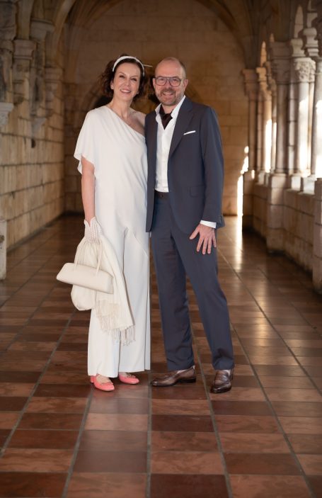 Couple in formal attire posing together in a historic stone corridor.