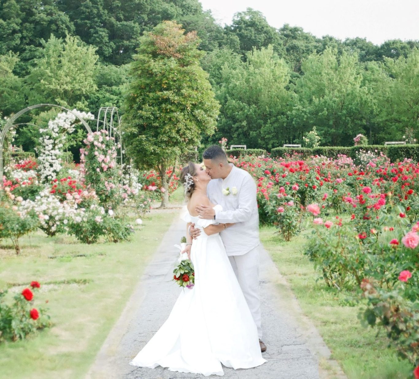 Bride and groom embrace in a rose garden, surrounded by lush greenery.