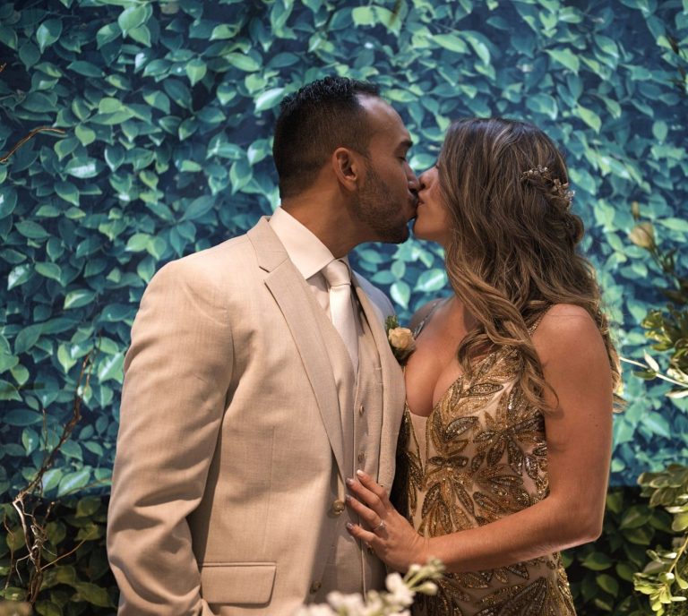 Engagement Photo Session Miami Couple kissing in formal attire, surrounded by greenery and floral arrangements.