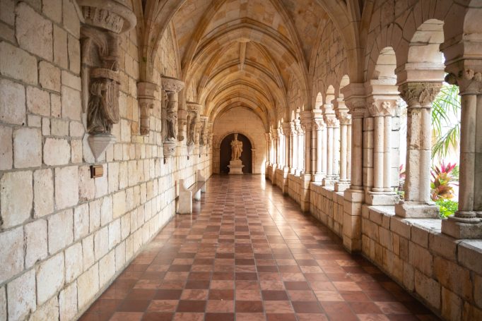 Stone corridor with arches and a statue at the end, featuring tiled flooring.