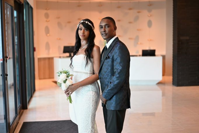 Bride and groom pose together in a modern venue, with the bride holding a bouquet.
