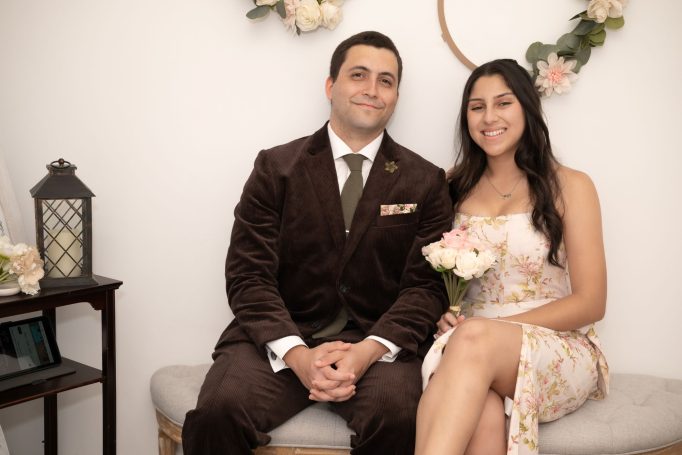 A couple dressed elegantly, smiling together with a bouquet of flowers.