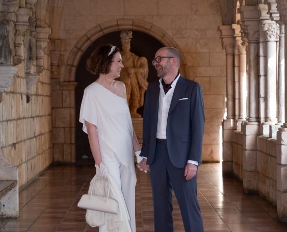 Bride and groom smiling while holding hands in a historic stone hallway.
