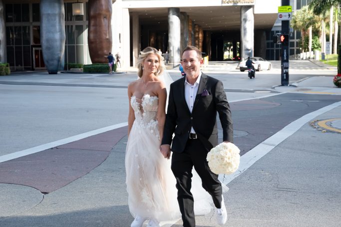 Bridal couple crossing the street, smiling and holding hands, with a city backdrop.