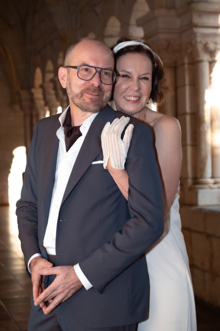 A happy couple poses together, the bride in a white dress and the groom in a dark suit.