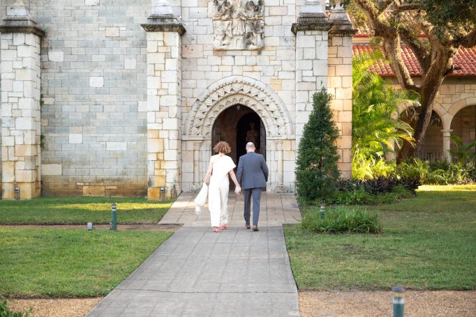 Couple walking towards a stone archway in a garden setting.
