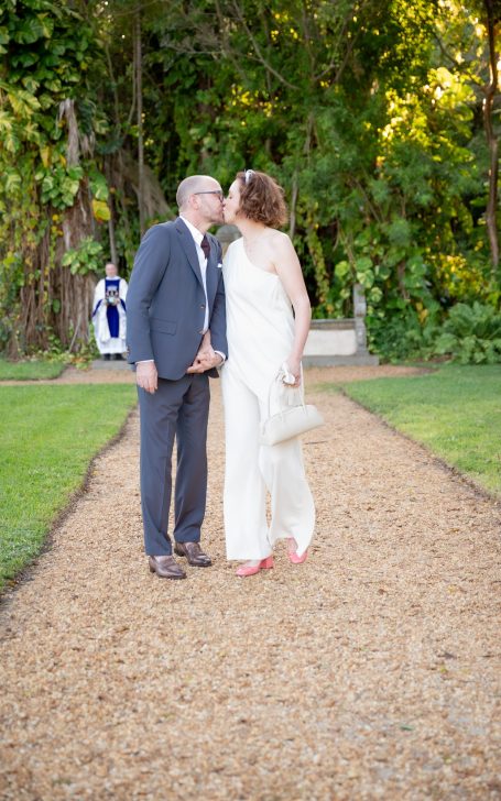Couple sharing a kiss on a path in a garden, surrounded by greenery.