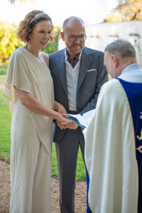 A couple exchanges vows during a wedding ceremony outdoors with an officiant.