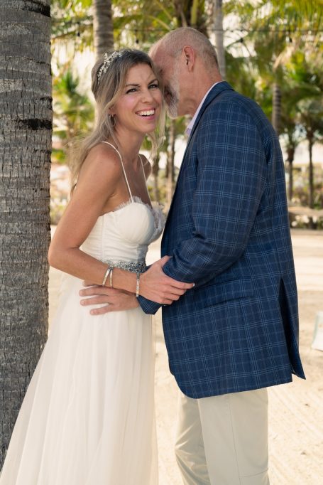 Bride and groom smiling together under palm trees on a beach.